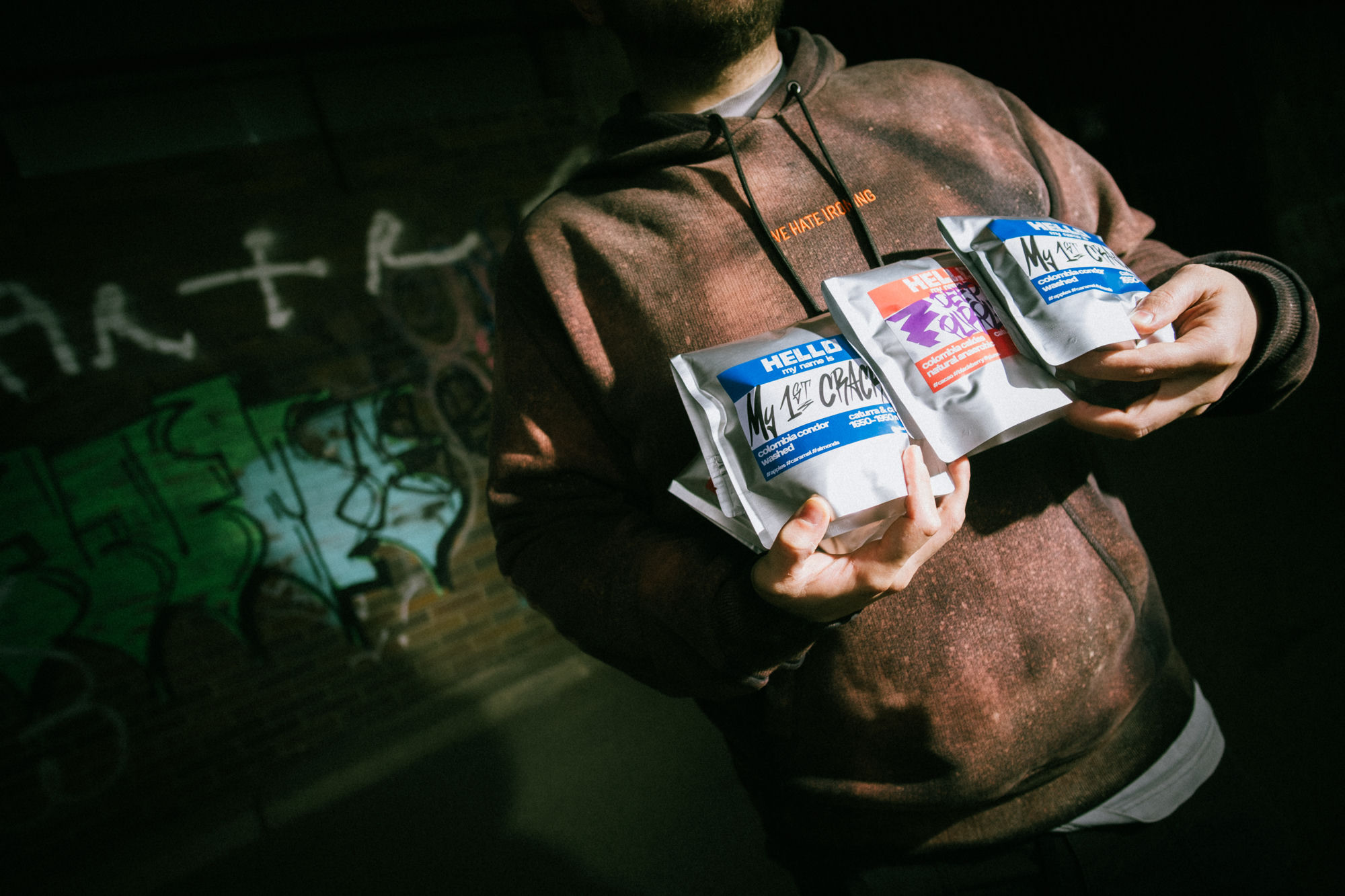 Three bags of Hello Roastery coffee held up in front of a graffiti wall